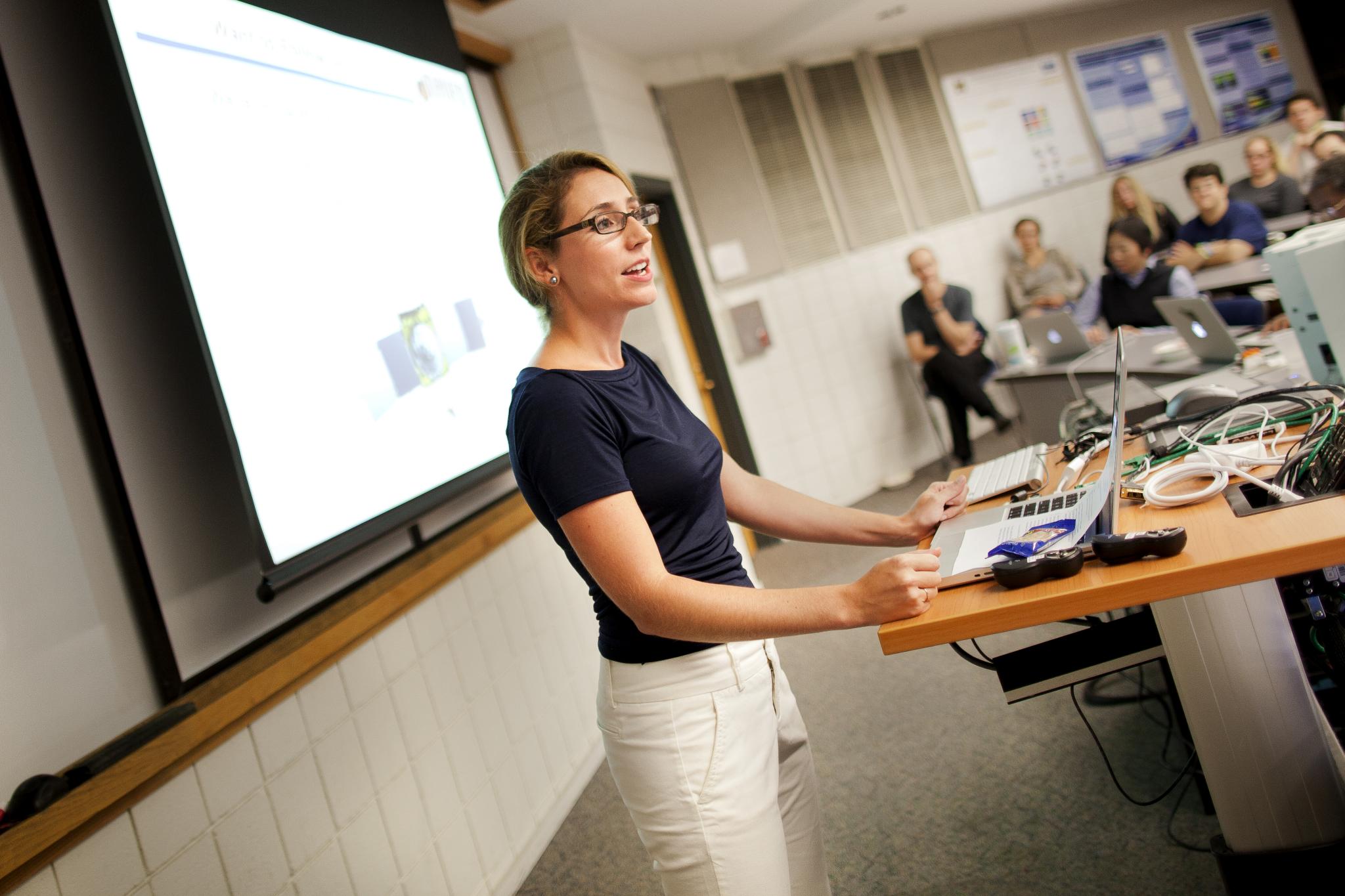 Woman stands in front of an audience in a lecture hall